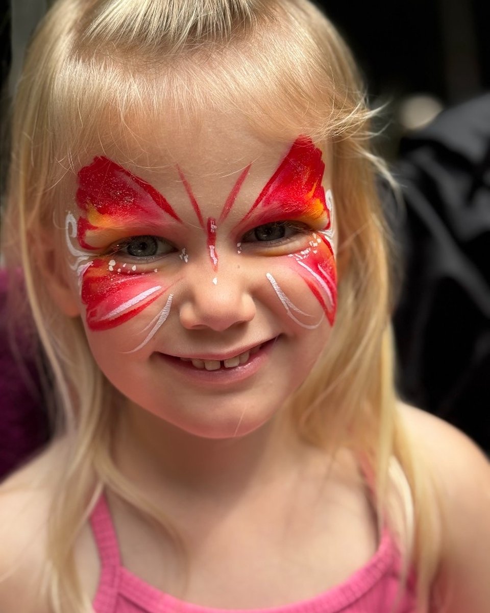 Smiling child with red and orange butterfly face painting by Wildflower Face Art