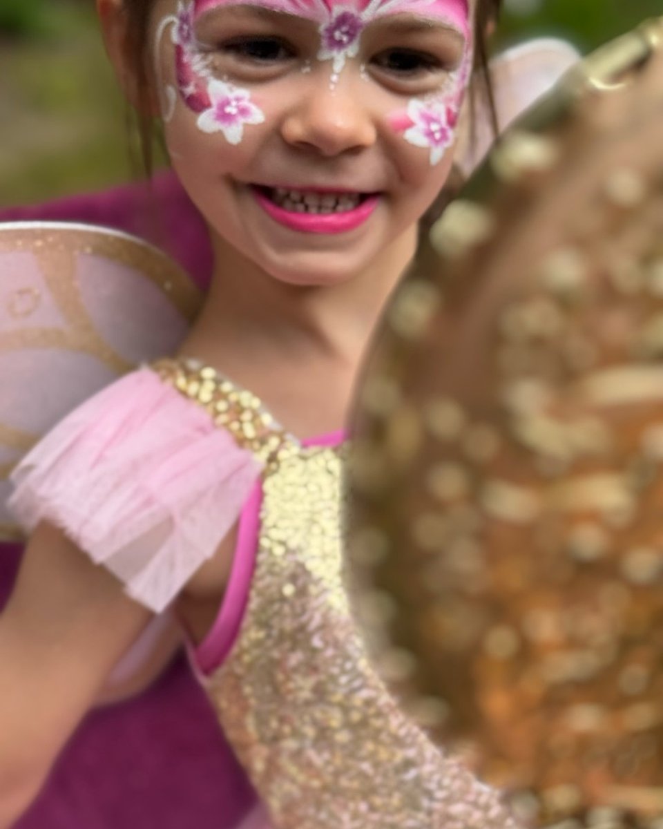 Child admiring fairy face painting in a mirror by Wildflower Face Art