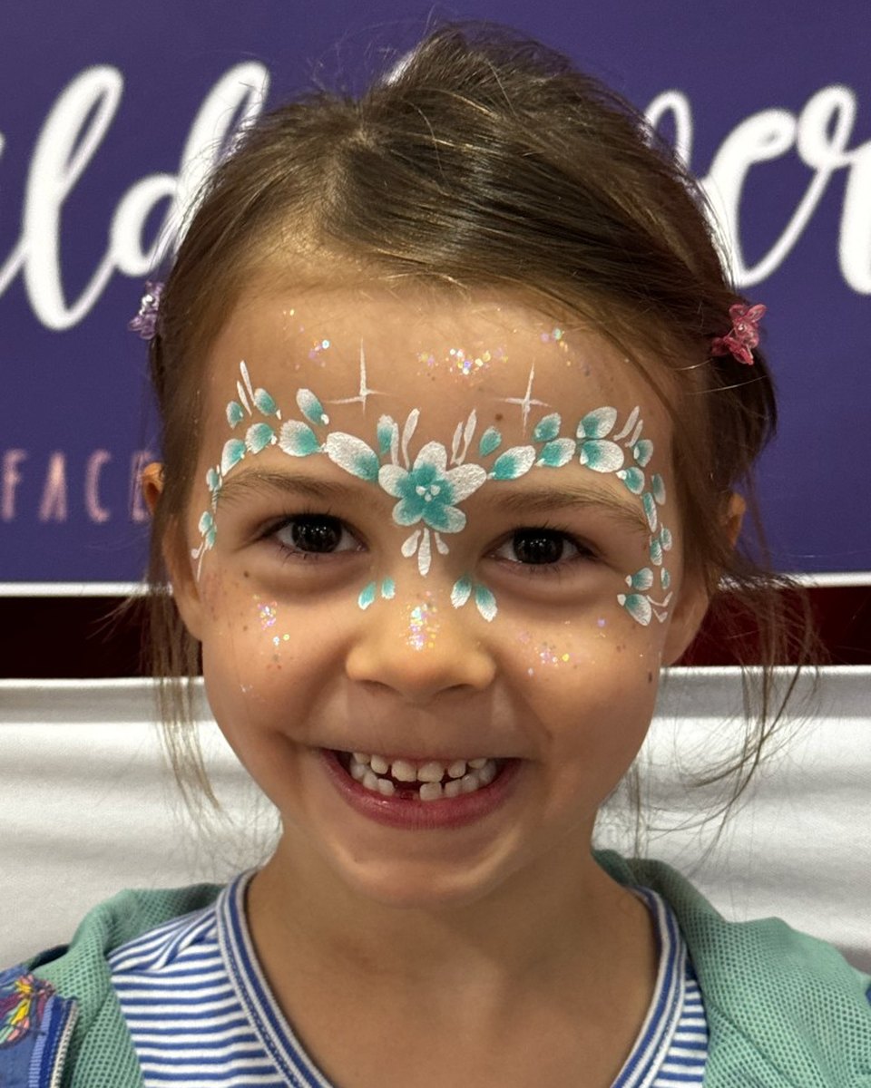 Smiling child with teal floral wreath face painting by Wildflower Face Art