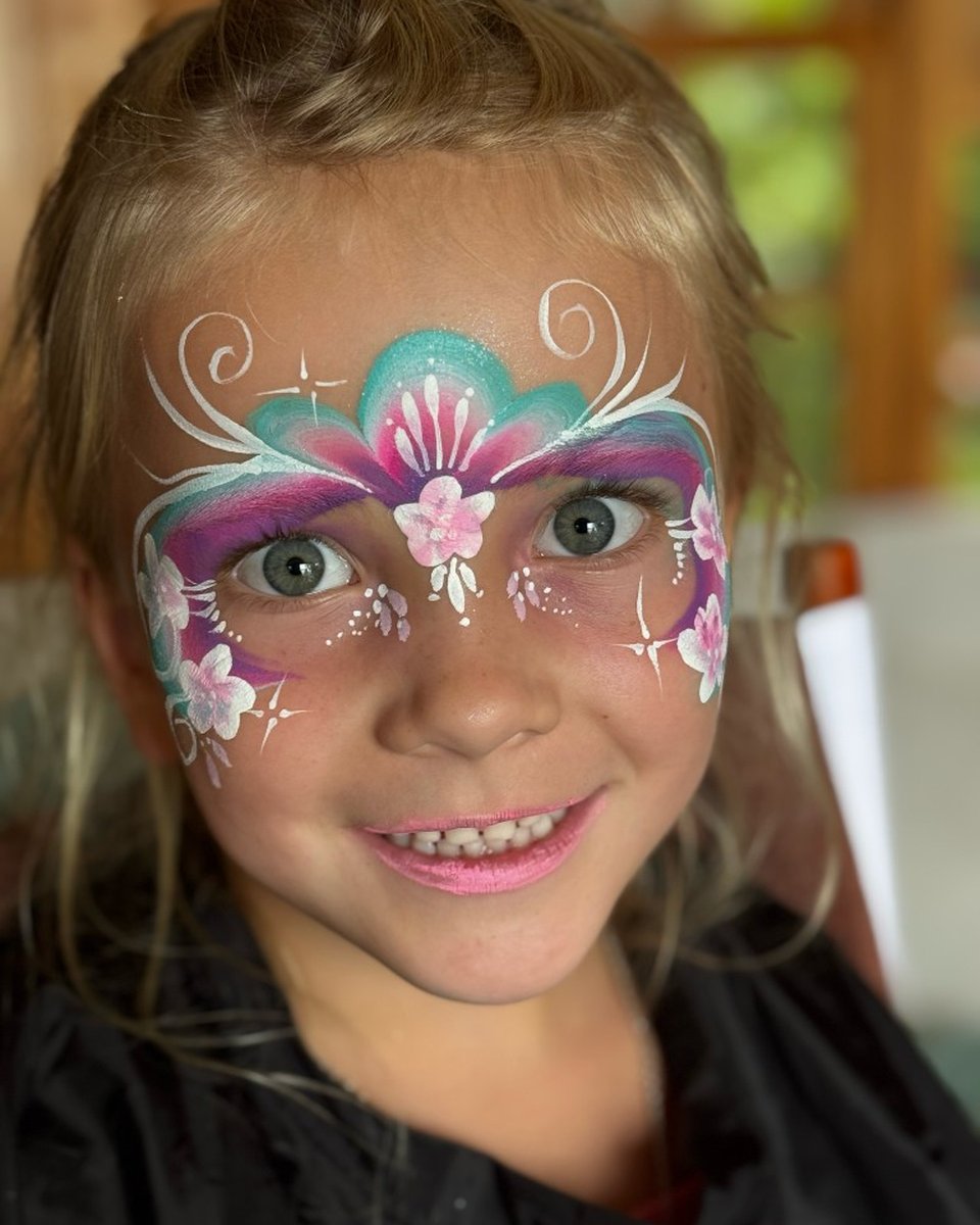Smiling child with teal and magenta floral crown face painting by Wildflower Face Art